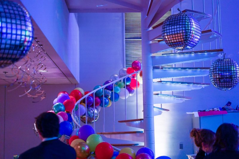 A blue-tinted photo of the spiral staircase in the Studio, lined with balloons and disco balls.