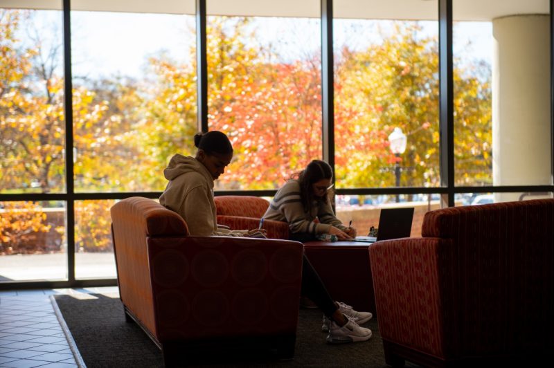 Two students work on the top floor of the Honors College Studio, set against a fall background outside.