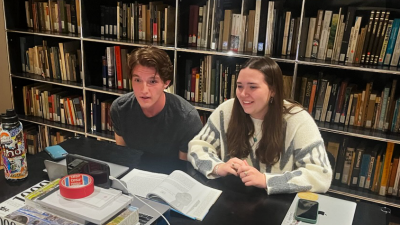 Eli Nichols and Emily Barcalow speak talk into the laptop while sitting in the Steger Center's library 