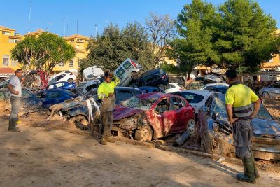 Workers in Spain look at muddy cars piled up on a street